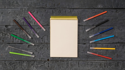 A set of markers and an open Notepad on a black wooden table.