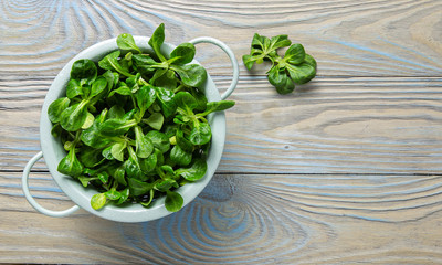 Fresh Corn salad leaves in colander on wooden background.Top view.Organic Mache Rosettes.