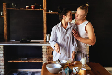 Beautiful young couple is smiling while cooking in kitchen at home