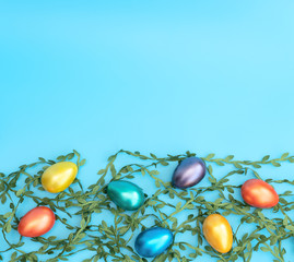 Decorated Easter eggs lie on green leaves on the blue background. Happy Easter holiday concept. Greeting, invitation card. Flat lay style with copy space.