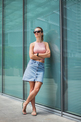 Young sexy woman in sunglasses posing near glass wall.