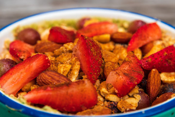 A smoothie bowl with oats, almond milk, almond yogurt, spinach, banana, berries, sliced strawberries, grapes topped with crushed almonds, almonds, Ezekiel cereal and a splash of cinnamon 