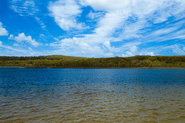 Tranquil lake and sky with clouds and green forests with trees