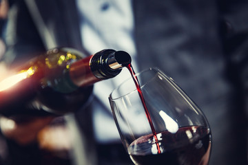 Red wine spouts into glass from bottle. Dark background