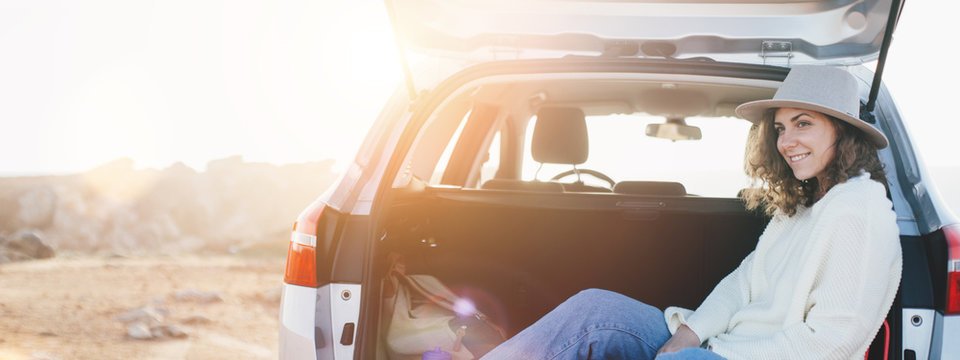 Young traveling woman sitting in the trunk of a car and resting, chilling stop on the nature. Intentional overexposed and lens flares