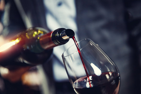 Red Wine Spouts Into Glass From Bottle. Dark Background