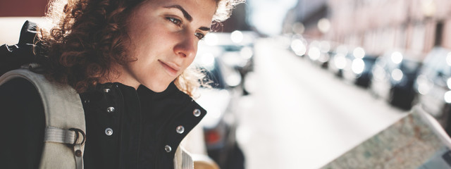 Handsome curly woman with backpack and big map walking around the city