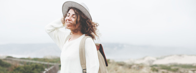 Happy woman with backpack and hat traveling among foggy park, natural reserve