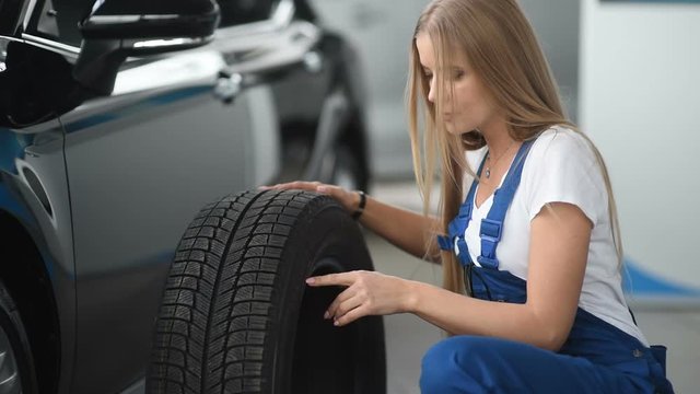 A mechanic woman rolls a new wheel for a car in a garage. Replacement of winter and summer tires.
