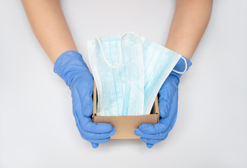 The doctor's caring hands in blue latex protective gloves hold a moving single open cardboard box containing protective face masks: medical concept, delivery concept, with medical care