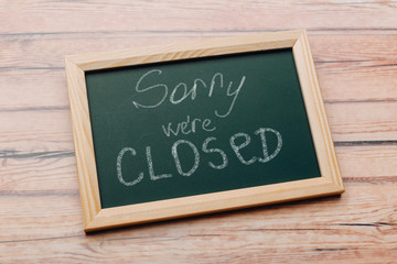Sign "Sorry, we are closed" on a chalk board with English inscriptions on a wooden