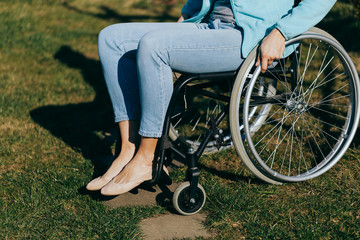 Obraz premium Close up of a young woman in a wheelchair while walking in a park on a sunny day. Recovery and healthcare concepts.