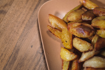 Baked crispy potatoes in a brown plate on a wooden table