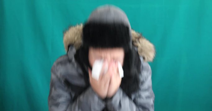 Winter portrait of young boy in warm clothes sneezing against chroma key green screen background