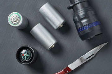 Old batteries near flashlight, knife and compass on dark concrete desk. Survival, tourism concept