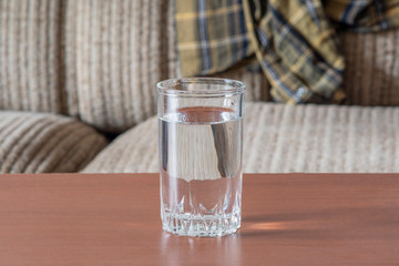 Glass cup with water on the table against the background of an old sofa.