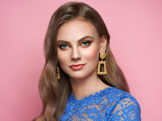 Fototapeta premium Brunette girl with perfect makeup. Beautiful model woman with curly hairstyle. Care and beauty hair products. Lady with fashionable gold makeup. Model with jewelry on pink background