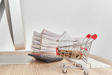 House on gold coins in shopping cart have blur calculator with pencil and pile report of sale on...