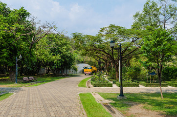 a truck sprays water green trees and plants in sunlight, in a park