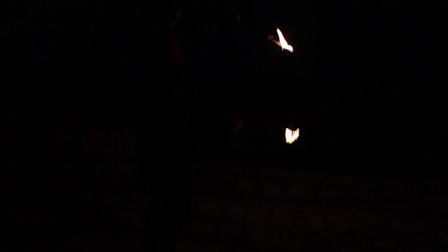 Professional juggler performing juggling tricks with 3 fire clubs, lighting the outdoor dark night scene. Slow motion shot.
