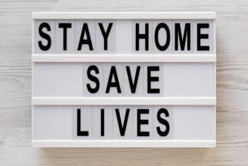 'Stay Home Save Lives' words on a lightbox on a white wooden surface, top view. Overhead, from above, flat lay.