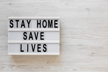 'Stay Home Save Lives' words on a lightbox on a white wooden background, top view. Overhead, from above, flat lay. Copy space.