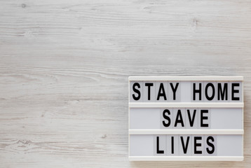 'Stay Home Save Lives' words on a lightbox on a white wooden background, top view. Overhead, from above, flat lay. Copy space.