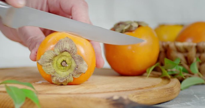 Men's hands cut the persimmon in half on a wooden cutting Board.