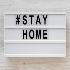 '#Stay home' words on a lightbox on a white wooden background, top view. Overhead, from above, flat lay.