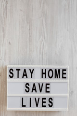 'Stay Home Save Lives' words on a lightbox on a white wooden background, top view. Overhead, from above, flat lay. Copy space.