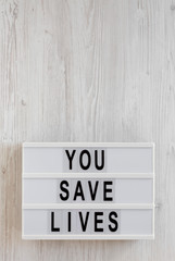 'You save lives' words on a lightbox on a white wooden background, top view. Overhead, from above, flat lay. Space for text.