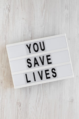 'You save lives' words on a lightbox on a white wooden surface, top view. Overhead, from above, flat lay.