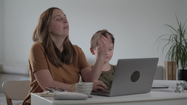 Mother and her son at home doing homework online with laptop. Remote education
