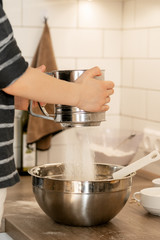 Close-up child's hands sifting flour into a large metal bowl. a boy in the kitchen preparing dough for baking