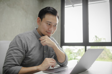 Happy face of Asian man working on laptop alone in the room.