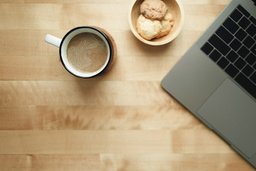 Top view of workspace with laptop and coffee cup on wooden desk.