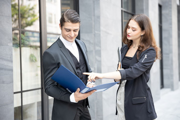 Two caucasian businessman explain project plan paperwork at group meeting standing at front office building in city.