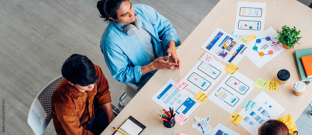 Poster Top view asian ux developer and ui designer brainstorming about mobile app interface wireframe design on table with customer breif and color code at modern office.Creative digital development agency