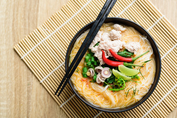 Spicy rice noodles soup with spices and herbs (Thai Tom Yum) in a bowl with chopsticks, Asian food, Top view