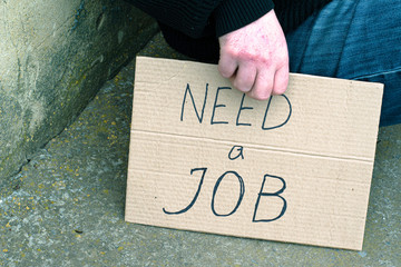 unemployed man sitting on the ground holding the cardboard sign saying need a job