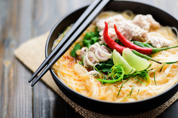 Spicy rice noodles soup with spices and herbs (Thai Tom Yum) in a bowl with chopsticks, Asian food