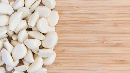 many peeled white cloves of garlic on a bamboo wooden cutting board. Right place for text.