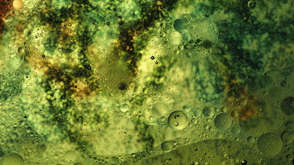 Mixing water and oil, beautiful colors. Close-up. Abstract background of filaments of different colors. Water and oil bubbles. Abstract green light illumination