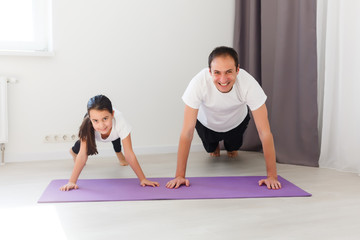 Father working out, doing single arm plank with his daughter. At home apartment.