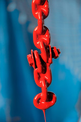 Vertical close-up of new chain link painted with red paint. Chain with paint drops, selective focus with blurred background. Toned to a film.