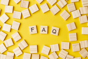Wooden blocks with abbreviation FAQ on the yellow background, top view. Frequently asked questions...