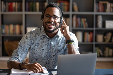 Happy young friendly african american man in eyeglasses wearing headset with mic, looking at...