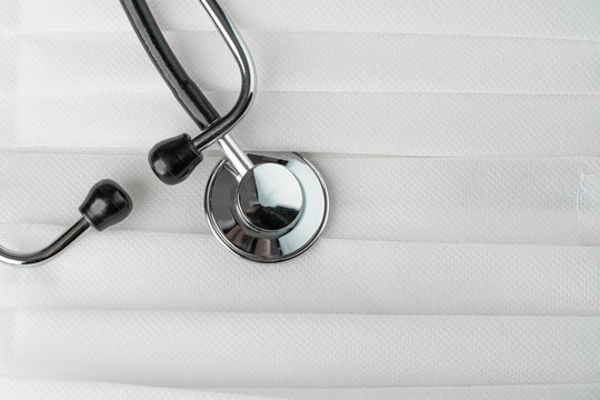 Medical stethoscope on a bunch of white protective face masks background. Copy space on the right.