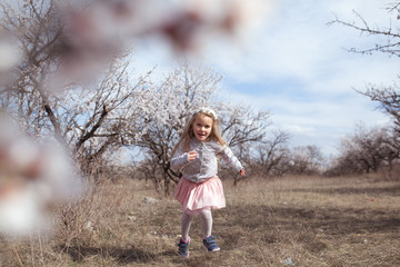 Happy beautiful girl runs in a flowering almond garden, outdoor