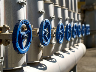 Phantom Blue industrial valves in a row on petrochemical plant pipelines system selective focus...